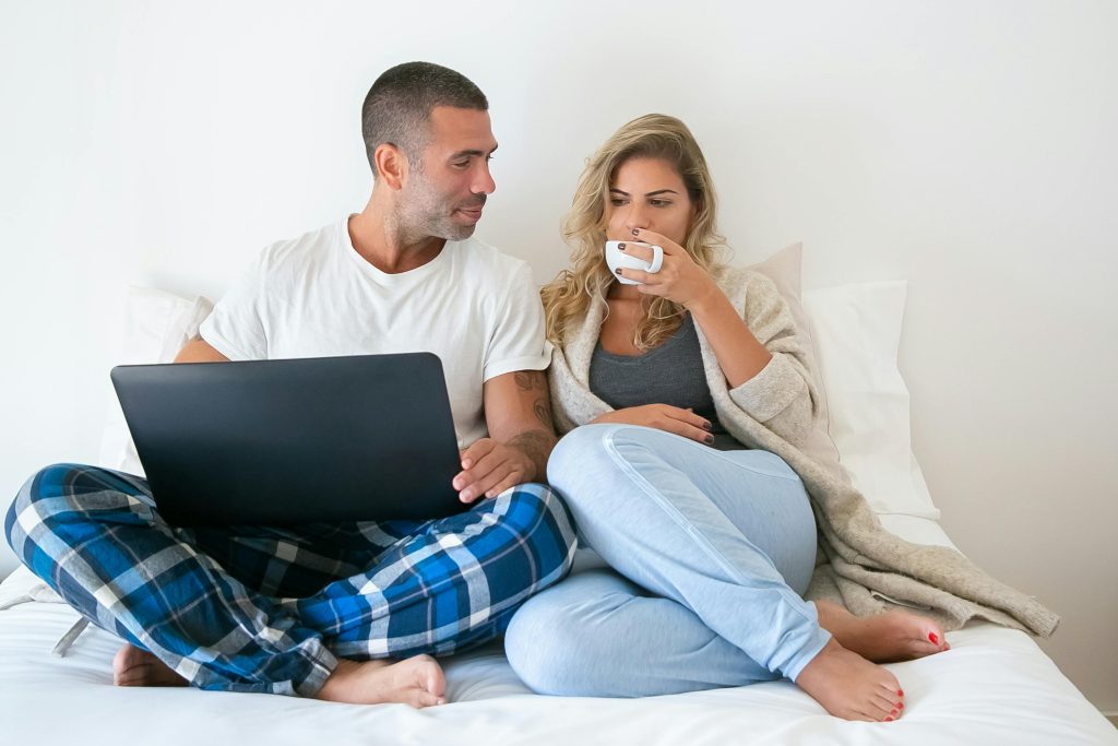 A midlife couple enjoying coffee and working on a laptop in bed, showcasing a cozy and relaxed work-from-home lifestyle